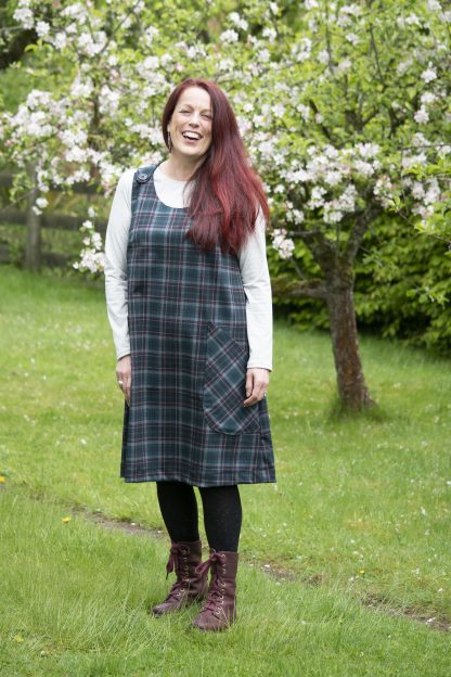 Woman wearing the Jayne Pinafore Dress sewing pattern from Bobbins and Buttons on The Fold Line. A dress pattern made in linen, medium weight denim or medium weight cotton fabrics, featuring an A-line silhouette, no zip, buttons at the shoulders, patch pockets and scoop neckline.