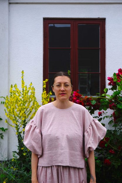 Woman wearing the ZW Soft Blouse sewing pattern from Birgitta Helmersson on The Fold Line. An oversized blouse pattern made in linen, cotton, silk or viscose fabrics, featuring dropped shoulders, gathered and twisted double layer sleeve, side bust darts, crew neck and a split with a loop and button centre back closure.
