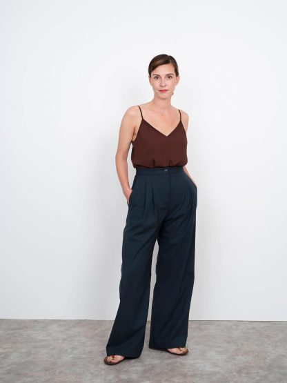 Woman wearing the High-Waisted Trousers sewing pattern from The Assembly Line on The Fold Line. A trouser pattern made in light to medium weight fabrics such as stretch wool, featuring a fitted high waist, straight waistband, fly zip, wide legs, slant front pockets, front pleats, and side tab detail in the back.