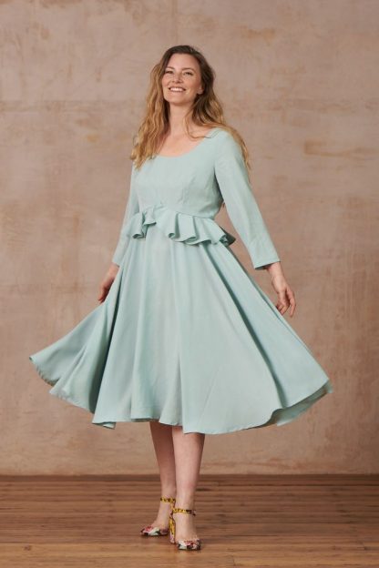 Woman wearing the Liz Dress sewing pattern from By Hand London on The Fold Line. A dress pattern made in viscose challis, crepe, silk twill, tencel, washed linen or brushed cotton fabrics, featuring a darted bodice, high waist, scoop neckline, full circle skirt with an inverted V waist and waistline flounce.