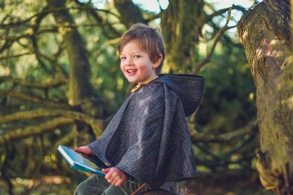 Child wearing the Baby/Child/Adult Storybook Cape sewing pattern from Waves & Wild on The Fold Line. A cape pattern made in wool blends, tweed and faux fur fabrics, featuring a hood and single toggle fastening.