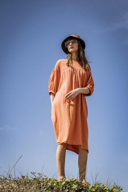 Woman wearing the Edda Dress sewing pattern from Fibre Mood on The Fold Line. A dress pattern made in gauze, poplin or lightweight cotton fabrics, featuring an oversized fit, jewel neck, dropped shoulders, balloon sleeves, side seam pockets, front and back yokes with gathers and midi length.