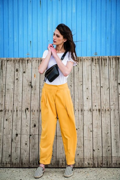 Women wearing the Onah Trousers sewing pattern from Fibre Mood on The Fold Line. A trouser pattern made in poplin, chambray, linen, baby wale corduroy or gabardine fabrics, featuring a waistband with asymmetrical fastening, pleats, pockets, zip and snap closure and just above ankle length.