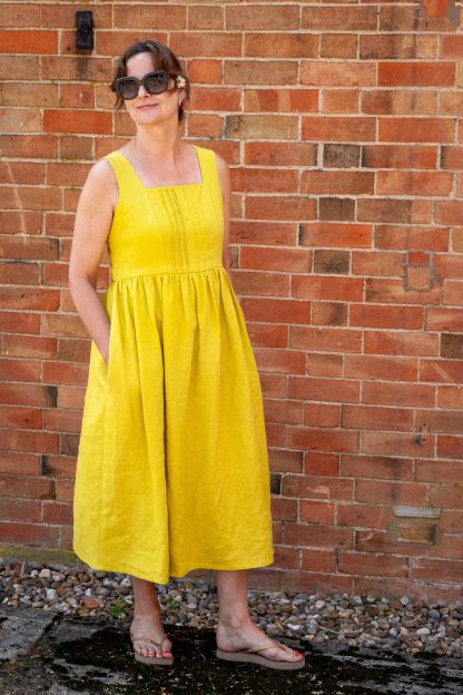 Woman wearing the Lavinia Dress sewing pattern from Sew Me Something on The Fold Line. A sleeveless dress pattern made in linen, viscose rayon, double gauze, cotton lawn or broderie anglaise fabrics, featuring a square neckline, shirred back with ties, broad shoulder straps, gathered high waist and midi length.