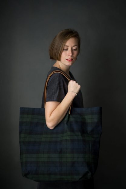 Woman holding the Orton Bag pattern from Merchant and Mills on The Fold Line. A tote bag pattern made in oilskin, dry oilskin, cotton canvas, drill, denim or linen fabrics, featuring an oversized silhouette and leather handles.