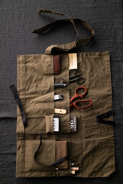 Photo showing the Tailor's Tool Roll pattern from Merchant and Mills on The Fold Line. A tool roll or tool apron pattern made in oilskin, dry oilskin, cotton canvas, drill or denim fabrics, featuring 15 assorted pockets and fabric strap.