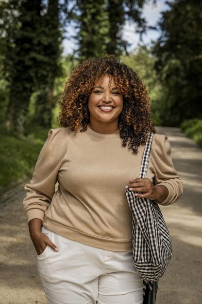Woman wearing the Clemence Top sewing pattern from Fibre Mood on The Fold Line. A jumper pattern made in knit fabric, knit jacquard, French terry, interlock or sweatshirt fabrics, featuring a round neck, long sleeves with cuffs, hem band, boxy shoulder gathers, and relaxed fit.