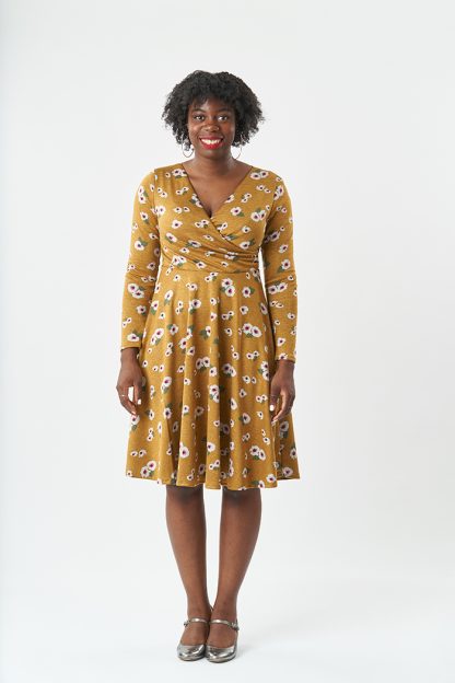 Woman wearing the Georgie Dress sewing pattern from Sew Over It on The Fold Line. A fit and flare knit dress pattern made in light to heavy weight knit fabrics, featuring a V-neck, wrap over bodice with pleats into the side seams, full-length set in sleeves, 3/4 circle skirt with elastic at the waist and knee length finish.