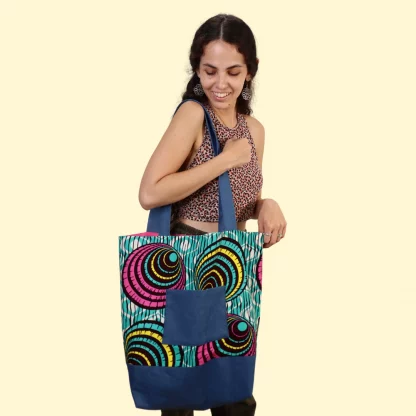 Woman holding the Madeline Tote Bag sewing pattern from Sirena Patterns on The Fold Line. A lined tote bag pattern made in novelty cotton, cotton blends or denim fabrics, featuring an oversized silhouette, patch pocket, shoulder straps and no closures.