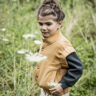 Child wearing the Micky Bodywarmer sewing pattern from Fibre Mood on The Fold Line. A bodywarmer pattern made in padded, quilted or sweatshirt fabrics, featuring a standing collar, snap closure, welt pockets and elasticated sleeve trim and hem band.