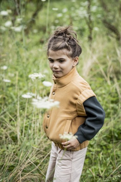 Child wearing the Micky Bodywarmer sewing pattern from Fibre Mood on The Fold Line. A bodywarmer pattern made in padded, quilted or sweatshirt fabrics, featuring a standing collar, snap closure, welt pockets and elasticated sleeve trim and hem band.