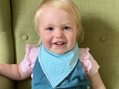 Child wearing the Bandana Bib sewing pattern from Waves & Wild on The Fold Line. A bib pattern made in cotton/bamboo velour, brushed cotton, quilting cotton or cotton/bamboo fleece fabrics, featuring a triangular shape with Velcro or snap closure.