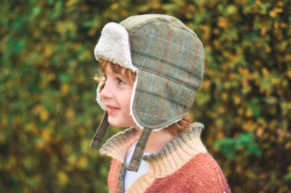 Child wearing the AJ Aviator Hat sewing pattern from Waves & Wild on The Fold Line. A hat pattern made in cord, wool, felt or denim fabrics, featuring ear flaps, chin straps and turned back peak.