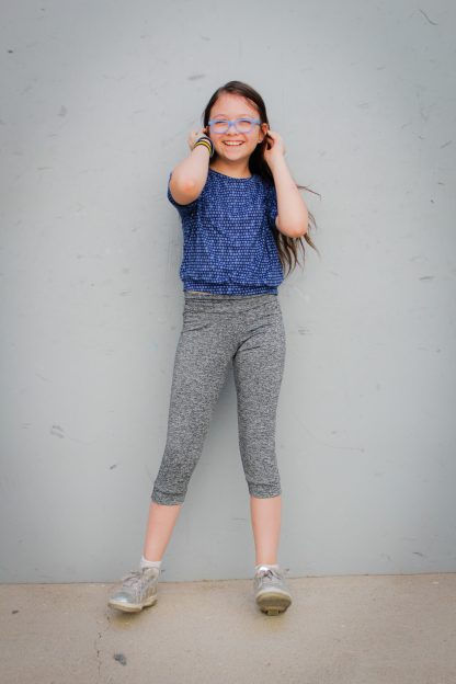 Child wearing the Lightning Leggings sewing pattern from Waves & Wild on The Fold Line. A leggings pattern made in cotton/lycra jersey fabrics, featuring a slim fit, cuffed waist and legs and capri length.