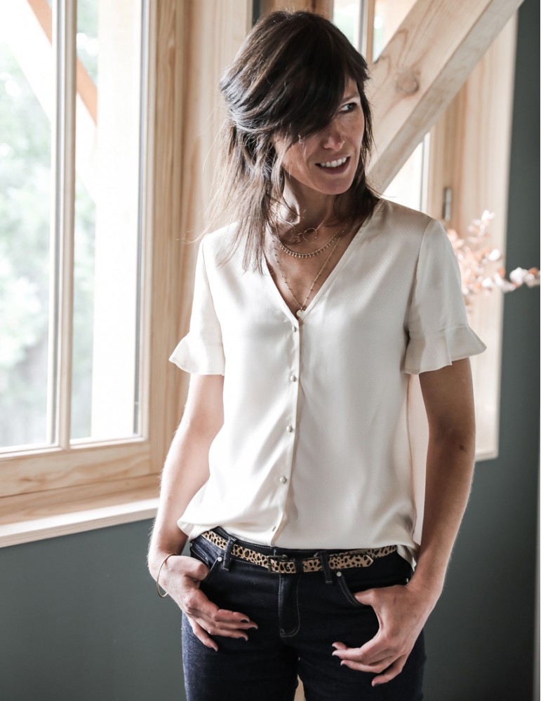 Woman wearing the Zoe Blouse sewing pattern from Atelier Scammit on The Fold Line. A relaxed fitting V- neck blouse pattern made in batiste, crêpe, double gauze or light denim fabrics, featuring a button placket and short sleeve with flared flounce.