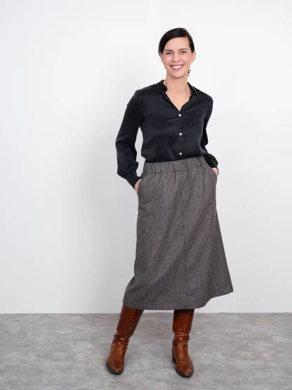Woman wearing the A-Line Midi Skirt sewing pattern from The Assembly Line on The Fold Line. A skirt pattern made in cotton poplin, denim, wool, faux leather or cotton twill fabrics, featuring an A-line silhouette, deep elasticated waistband, side slant pockets, straight hemline and mid-calf length.