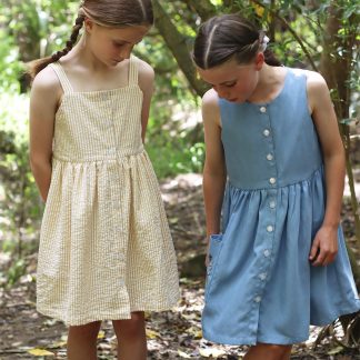Children wearing the Baby/Child/Teen Rimu Dress sewing pattern from Below the Kowhai on The Fold Line. A relaxed fitting, sleeveless dress pattern made in chambray, lawn, linen, rayon, seersucker, tencel, viscose and voile fabrics, featuring front button closure, fully lined bodice with straps or sleeveless bodice, and in-seam or patch pockets.