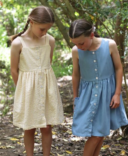 Children wearing the Baby/Child/Teen Rimu Dress sewing pattern from Below the Kowhai on The Fold Line. A relaxed fitting, sleeveless dress pattern made in chambray, lawn, linen, rayon, seersucker, tencel, viscose and voile fabrics, featuring front button closure, fully lined bodice with straps or sleeveless bodice, and in-seam or patch pockets.