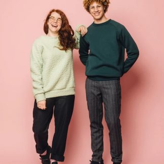 Man and women wearing the Maggi Sweater sewing pattern from Melilot on The Fold Line. A unisex sweater pattern made in ponte, double knit, sweatshirt fleece, french terry, jersey or sweater knit fabrics, featuring a relaxed fit, raglan sleeves, cuff, neck and hem bands, full length sleeves plus shorter or longer length.