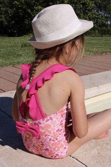 Child wearing the Children's Poéma Swimsuit pattern from Etoffe Malicieuse on The Fold Line. A lined swimsuit pattern made in swimsuit fabric such as lycra with four way stretch, featuring a rounded back, crossed straps with flounces, shoulder flounces, low leg rise, and V-neck.