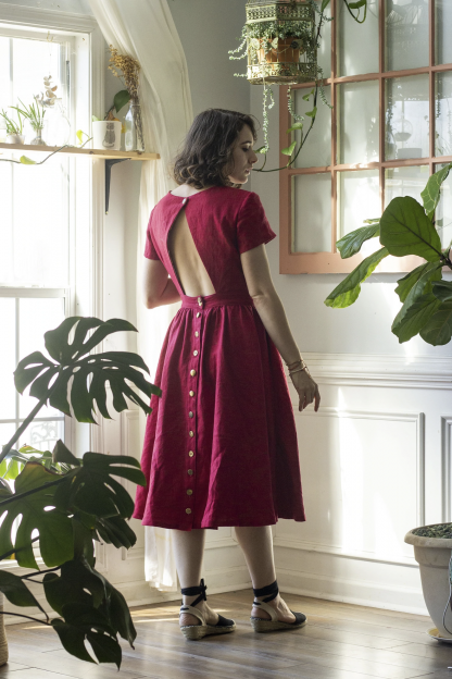 Woman wearing the Amélie Dress sewing pattern from Untitled Thoughts on The Fold Line. A dress pattern made in chambray, silk noil, lightweight linen, tencel, quilting cotton, flannel or mid-weight denim fabrics, featuring a back button skirt, patch pockets, tea length hem, completely open back closed by single neck button, slender bicep sleeves and bust cup options.
