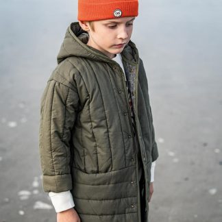 Child wearing the Child/Teen Bobby Jacket sewing pattern from Fibre Mood on The Fold Line. A jacket pattern made in padded, quilted, matelassé, faux fur, teddy or wool fabrics, featuring front snap fasteners, coat length, hood and full length sleeves.