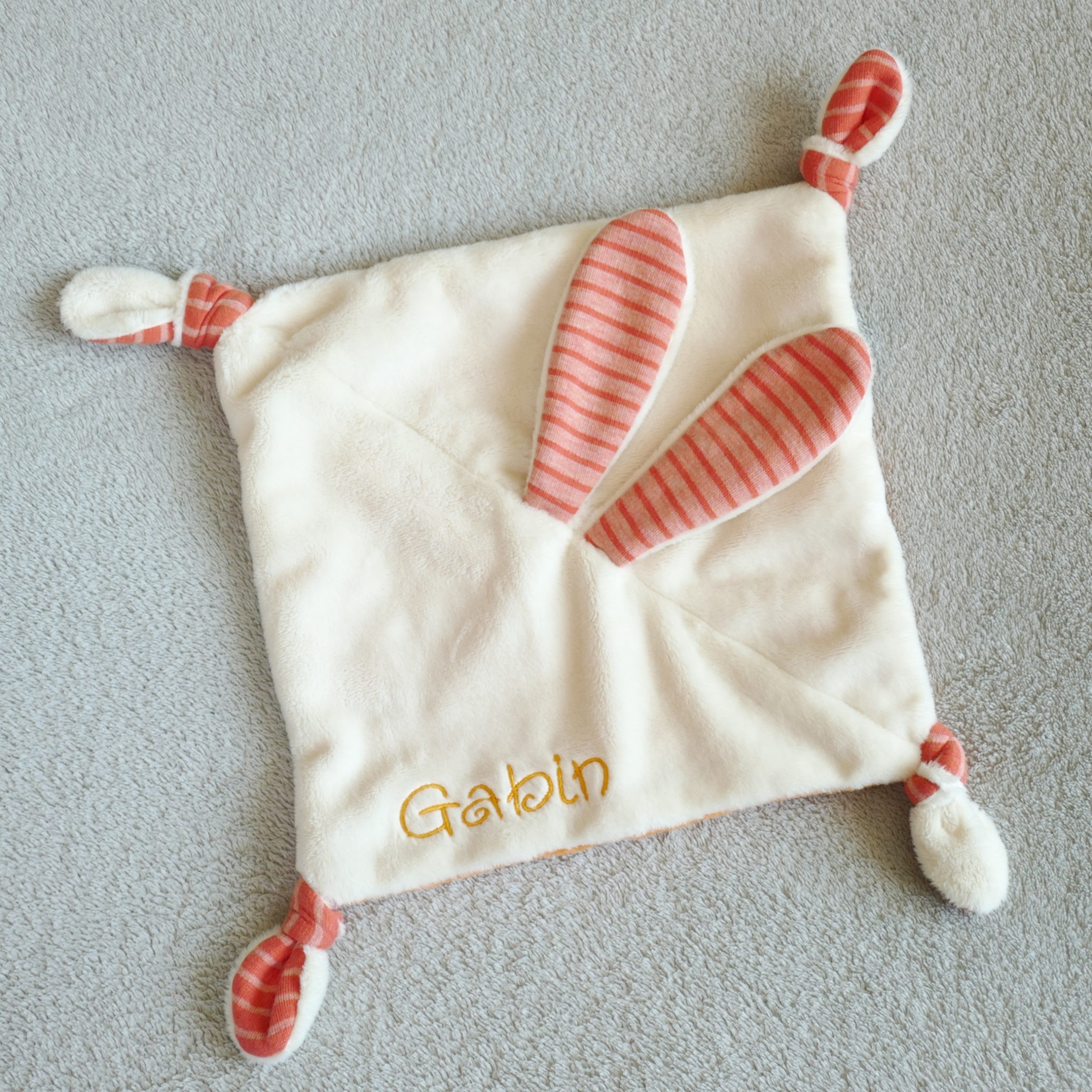 Photo showing the Bunny Lovey Baby Comforter sewing pattern from Petits D'om on The Fold Line. A comforter pattern made in minky or plush fabrics, featuring a square of fabric with bunny ears in the centre and knotted corners.