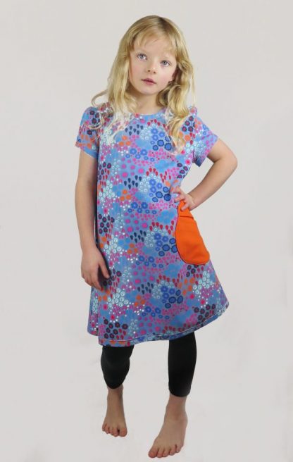 Child wearing the Children's Playtime Swing Dress sewing pattern from Ruth Maddock Makes on The Fold Line. A dress pattern made in jersey fabrics, featuring a pull over the head style, round neck, set–in short sleeves, patch pockets and straight hem.