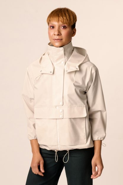 Woman wearing the Sirkka Hooded Jacket sewing pattern from Named on The Fold Line. A jacket pattern made in light outerwear fabrics, featuring a detachable hood, long sleeves, zip closure with zipper shield and snap button closure, high collar, large patch pockets, side pocket, overlapping pocket flaps with snaps, hood, hemline and cuffs are gathered with elastic cords.
