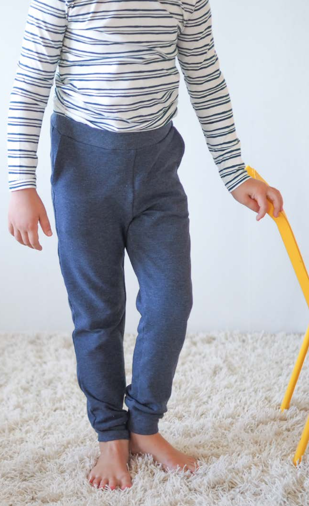 Child wearing the Children's Fieldfare Joggers sewing pattern from Pattern by Malena on The Fold Line. A joggers pattern made in medium weight knit fabrics, featuring an elasticated waistband, wide ankle cuff, front angled pockets and relaxed fit.