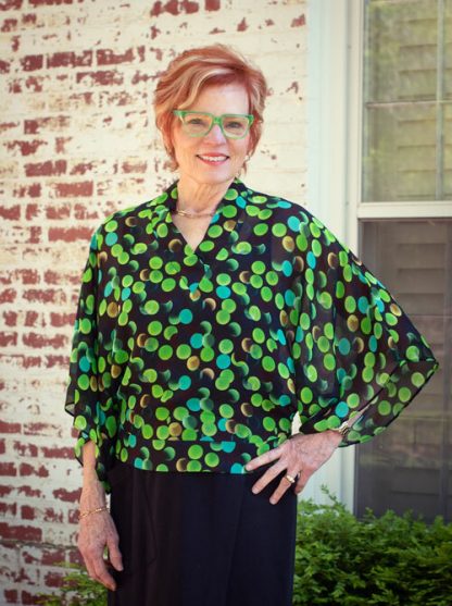 Woman wearing the Coco Blouse sewing pattern from The Sewing Workshop on The Fold Line. A top pattern made in crepe de chine, lightweight cotton, cotton voile, lightweight linen, rayon or light to mid-weight knit fabrics, featuring a loose-fitting bodice, side seam zipper, inset V-neck, collar and hip band, front and back extend into elbow-length sleeves.