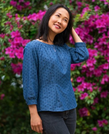 Woman wearing the Galicia Top sewing pattern from Itch to Stitch on The Fold Line. A blouse pattern made in lightweight linen, chambray, lawn, crepe, shirting or challis fabrics, featuring front neckline gathers, raglan sleeves, back button closure, 3/4 sleeves with button cuffs, front and back waist darts and shirt tail hem.