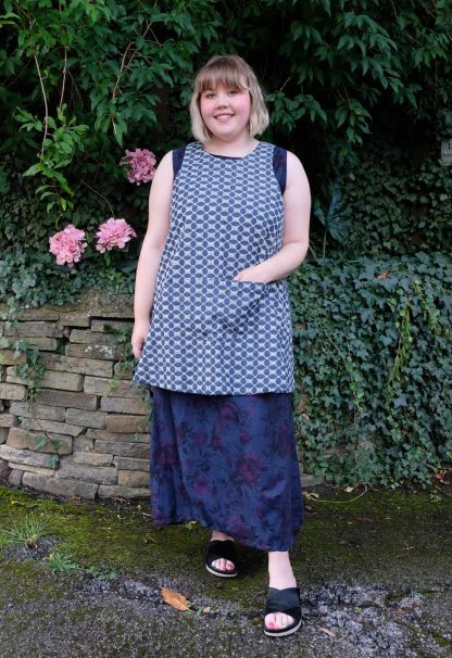 Woman wearing the Herba Apron sewing pattern from Sew Different on The Fold Line. An apron pattern made in cotton, linen, denim or needlecord fabrics, featuring a crossed back design that pulls on over the head, large front pocket, scalloped back hem and round neckline.