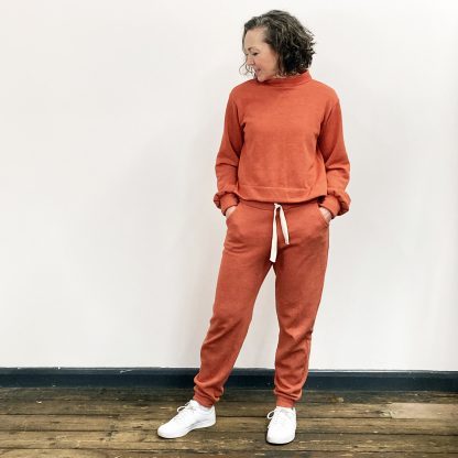 Woman wearing the Homebody Joggers sewing pattern from My Handmade Wardrobe on The Fold Line. A joggers pattern made in sweatshirt, fleece, velour or French terry fabrics, featuring a slim straight leg, elasticated waistband with drawstring, front pockets, fitted ankle cuff and relaxed loose fit.