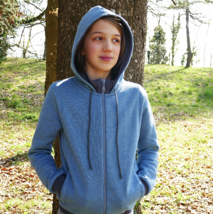 Child wearing the Child/Teen Keefe Sweatshirt sewing pattern from Petits D’om on The Fold Line. A hoodie pattern made in sweatshirt fabric such as brushed, fleece, jogging fabric or French terry fabrics, featuring centre front zip closure, full length sleeves with cuffs, hood with drawstring closure, pockets and relaxed fit.