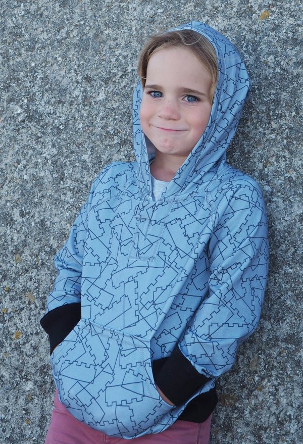 Child wearing the Children's Playtime Raglan Hoodie sewing pattern from Ruth Maddock Makes on The Fold Line. A hoodie pattern made in jersey fabrics, featuring raglan sleeves, centre front opening with tab, hood, front pocket and contrast ribbed waistband and cuffs.