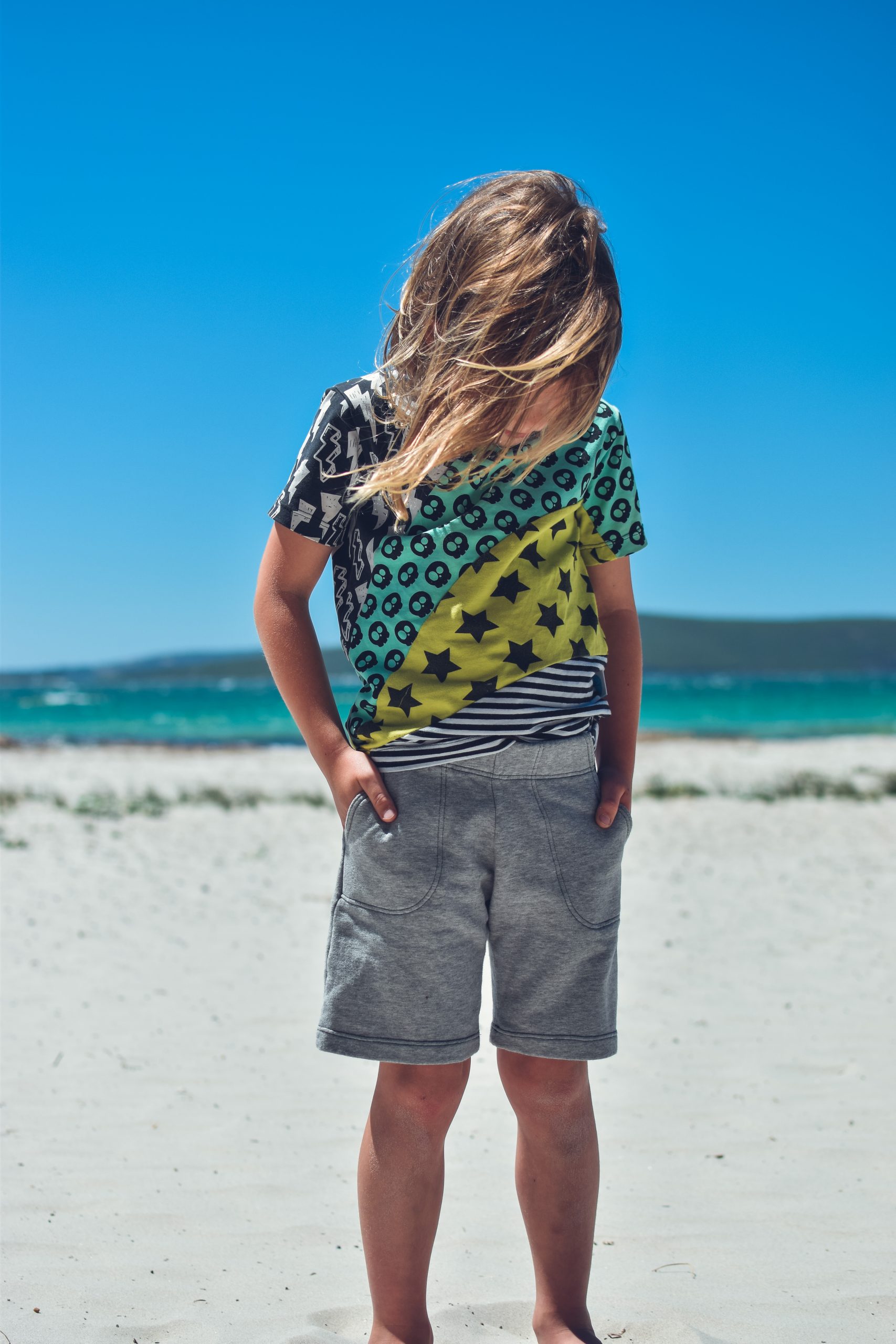 Child wearing the Baby/Child Shoreline Shorts sewing pattern from Waves & Wild on The Fold Line. A shorts pattern made in French terry or sweatshirt fleece fabrics, featuring knee length, elasticated waist, front angled pockets and relaxed fit.