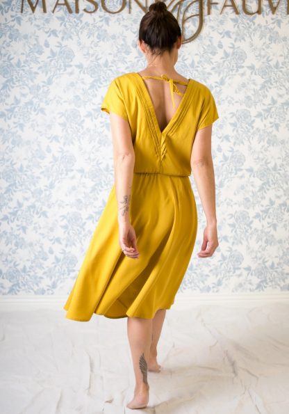 Woman wearing the Byzance Dress sewing pattern from Maison Fauve on The Fold Line. A skater dress pattern made in viscose, broderie anglaise, tencel, soft and light cotton, linen or crepe fabrics, featuring a v-neckline at the front and back emphasised by pleats and held in place with ties at the back, elasticated waist gathered at the front, grown on short sleeves, relaxed fit and knee length finish.