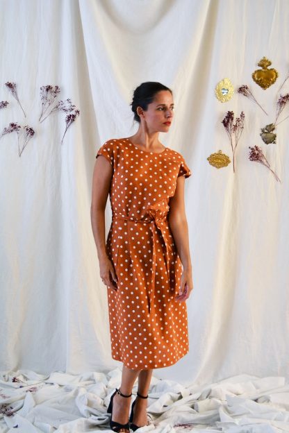 Woman wearing the Leaf Dress sewing pattern from Maison Fauve on The Fold Line. A dress pattern made in viscose, cotton, satin, crepe or lace fabrics, featuring a round neck at the front, back crossover V-neckline, bust darts, grown-on cap sleeves, midi length, waist pleats` and self-fabric belt.