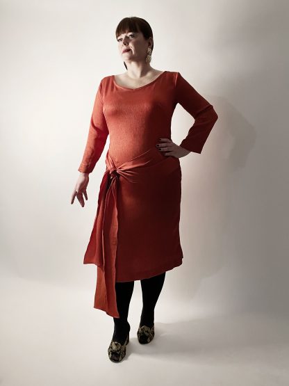 Woman wearing the No. 25 Penhouët Dress and Top sewing pattern from How to Do Fashion on The Fold Line. A dress pattern made in stretch knit or woven fabrics, featuring a fitted pencil dress silhouette, long sleeves, scoop neck, back vent, waist tie and just below knee length.