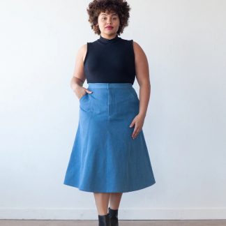 Woman wearing the Salida Skirt sewing pattern from True Bias on The Fold Line. A panelled skirt pattern made in denim, twill, corduroy, linen or chambray fabrics, featuring a front and back V-shaped yoke, high waist, front zipper fly, mid-calf length and flares out at the bottom.