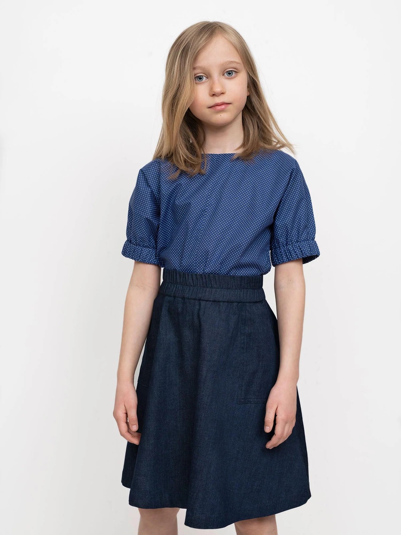 Child wearing the Children's Elastic Waist Skirt Mini sewing pattern from The Assembly Line on The Fold Line. A skirt pattern made in light to mid-weight fabrics, featuring an elasticated waistband, relaxed fit, large patch pockets and knee length finish.