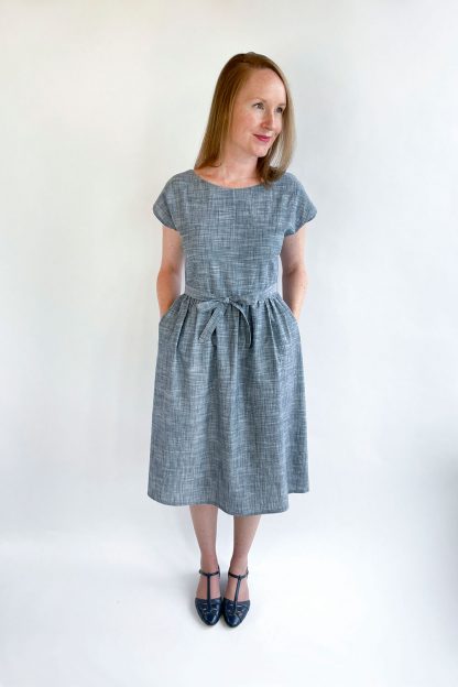 Woman wearing the Isla Wrap Dress sewing pattern from Jennifer Lauren Handmade on The Fold Line. A wrap dress pattern made in cotton lawn, voile, poplin, linen, light chambray, denim, sateen, rayon, silks or crepes fabrics, featuring waistline darts, grown-on sleeves, rounded neckline, gathered skirt, in-seam pockets, below knee length hem, back-wrap bodice is angled from the centre back neckline to the waist and waist ties close the dress.