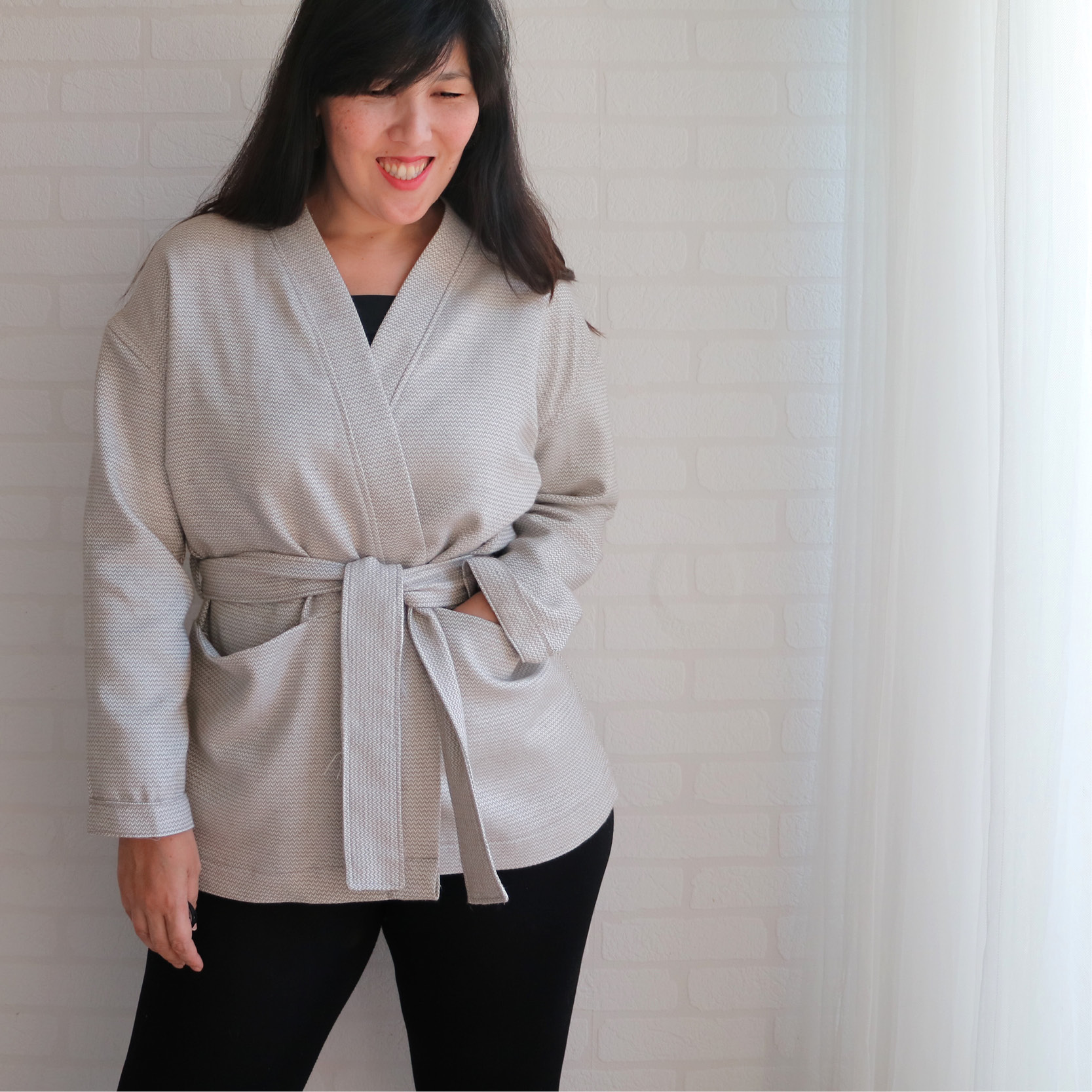 Woman wearing the Komi Jacket sewing pattern from Wardrobe by Me on The Fold Line. A wrap jacket pattern made in medium weight woven or jersey, featuring deep pockets, wrap front held in place by a belt and dropped shoulders with cuff at the hem.