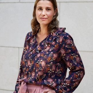 Woman wearing the Liv Blouse sewing pattern from Atelier Jupe on The Fold Line. A blouse pattern made in viscose or tencel fabrics, featuring a loose-fit, V-neckline, ruffle at the front neckline, back yoke with gathers and long sleeves with elasticated hem.