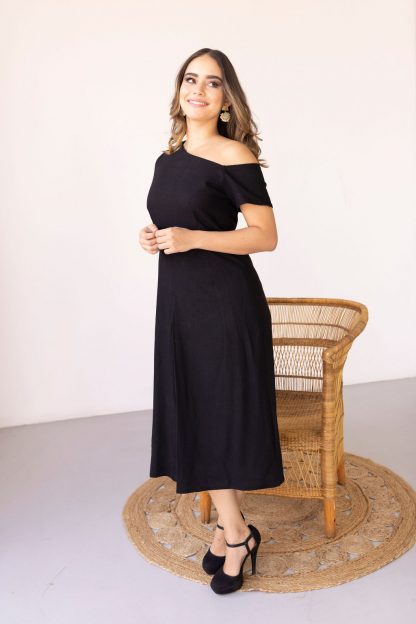 Woman wearing the Mila Dress sewing pattern from Pattern Sewciety on The Fold Line. A dress pattern made in cotton, cotton blends, linen, linen blends, rayon or satin fabrics, featuring an asymmetric neckline, front and back waist darts, invisible back zipper, box pleat midi skirt, one short sleeve, and an off-the-shoulder sleeve.