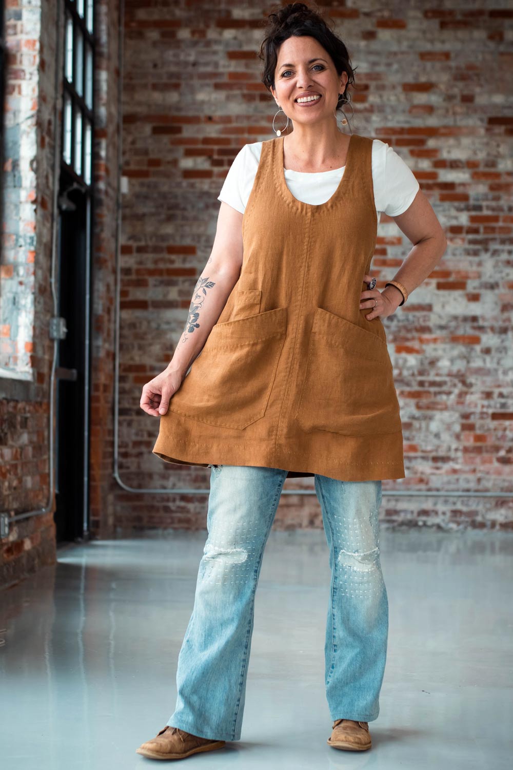Woman wearing the Studio Tunic sewing pattern from Sew Liberated on The Fold Line. A pinafore tunic pattern made in mid-weight linen, chambray, cotton twill or light canvas fabrics, featuring roomy pockets, deep scoop neck, low armholes, A-line silhouette and mid-thigh hem.