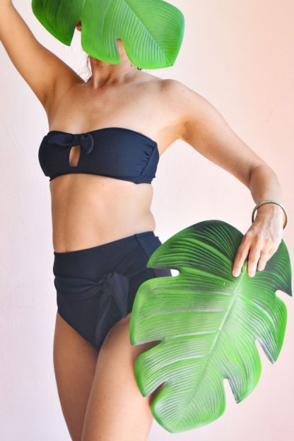 Woman wearing the Cuba Libre Bikini sewing pattern from Fitiyoo on The Fold Line. A bikini pattern made in two-way stretch fabrics, featuring a bandeau bra with central cut-out and high-waisted briefs with front, self-fabric tied knot.