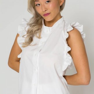 Woman wearing the Adela Blouse sewing pattern from Bara Studio on The Fold Line. A sleeveless blouse pattern made in viscose, cotton linen or tencel fabrics, featuring ruffles, small stand collar and button placket.