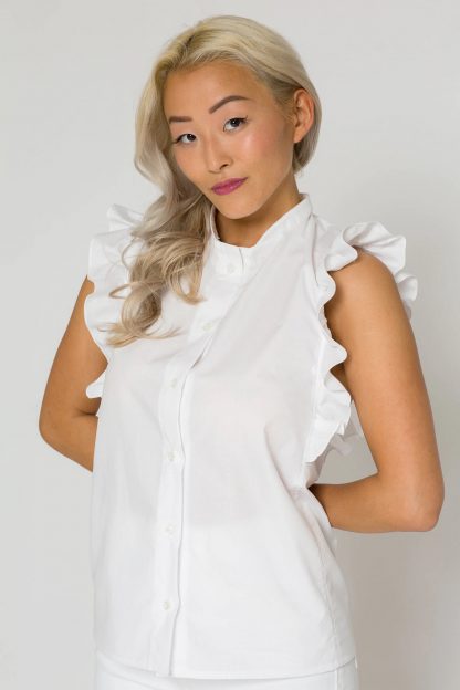 Woman wearing the Adela Blouse sewing pattern from Bara Studio on The Fold Line. A sleeveless blouse pattern made in viscose, cotton linen or tencel fabrics, featuring ruffles, small stand collar and button placket.